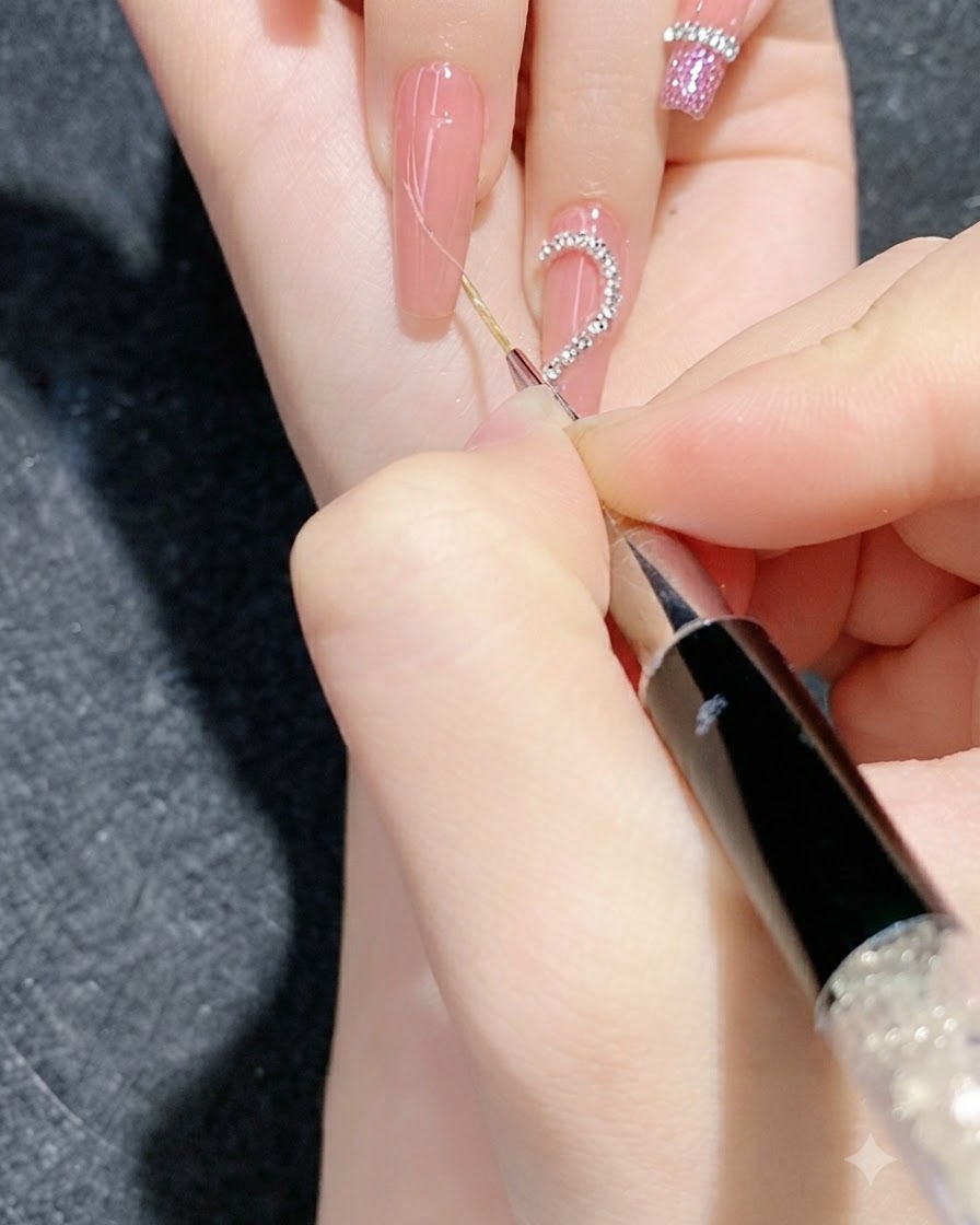 A close-up view of a detailed nail art session using a fine tool to press rhinestone chain strips onto a gradient nail.