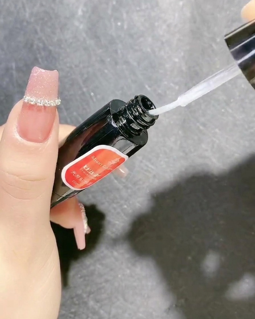 A bottle of clear sealing gel with a brush applicator being used to secure nail decorations.