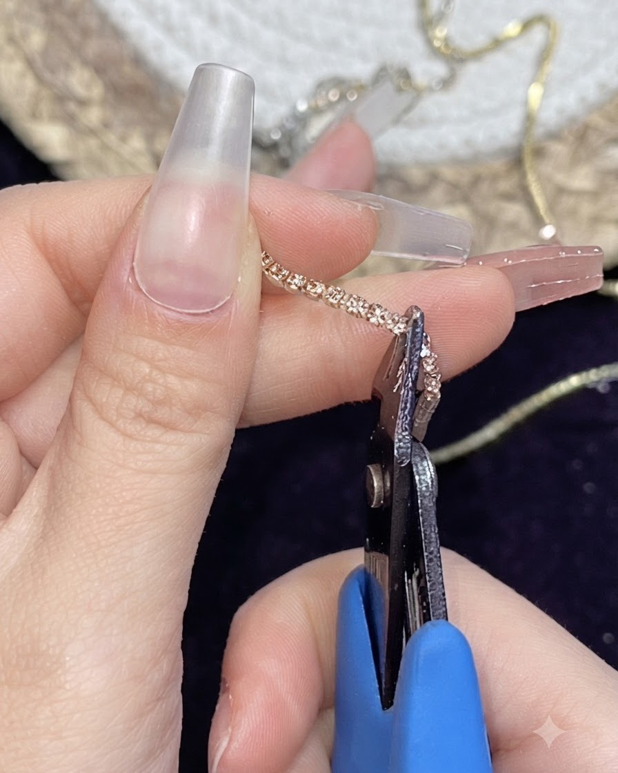 A pair of small metal nippers cutting a metallic gold chain strip held between fingers.
