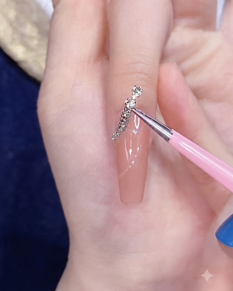 A fine applicator tool placing a segmented silver-gold chain strip onto the curved line of a nail.