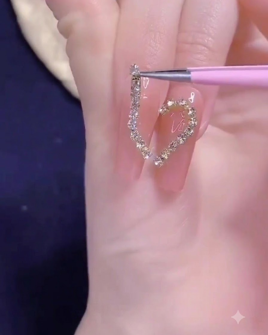 A pair of precision tweezers placing a golden chain strip onto the half-heart nail design.