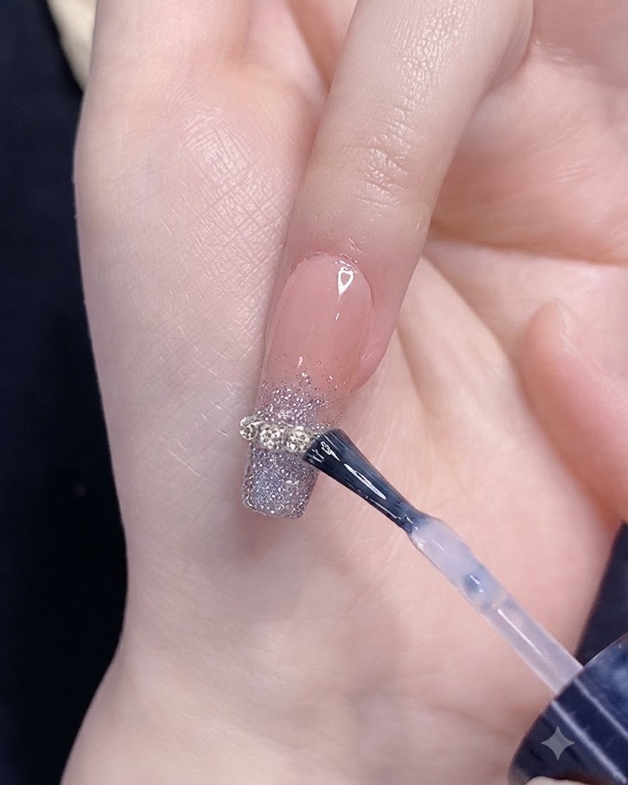 A brush applying top coat over a silver glitter gradient nail with a chain strip accent.