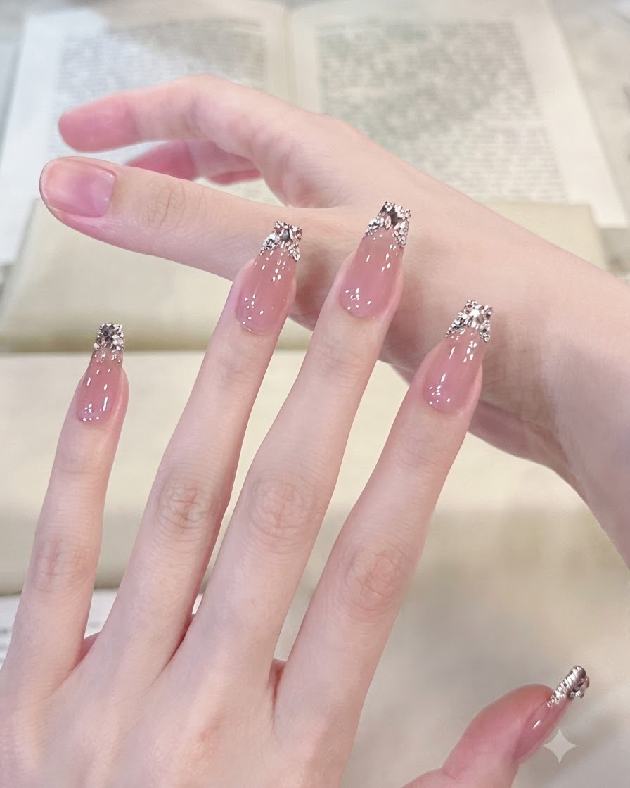 Macro shot focusing on a manicured thumb and index finger highlighting detailed silver glitter fading and arranged crystal gems.