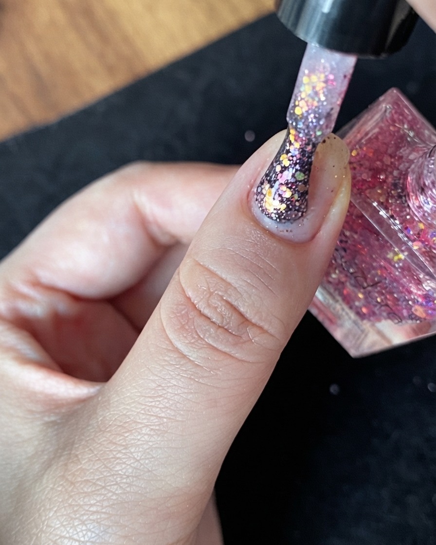A close-up view of a natural nail with a nude base layer and sparse scattered glitter flakes.