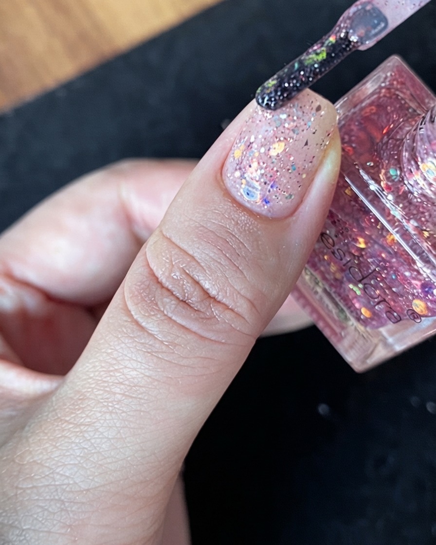 A generous cluster of multicolored glitter flakes placed directly in the center of a nude nail.
