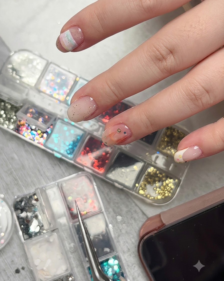 A pair of tweezers holding a tiny star glitter piece just above a decorated nail surface with various accents.