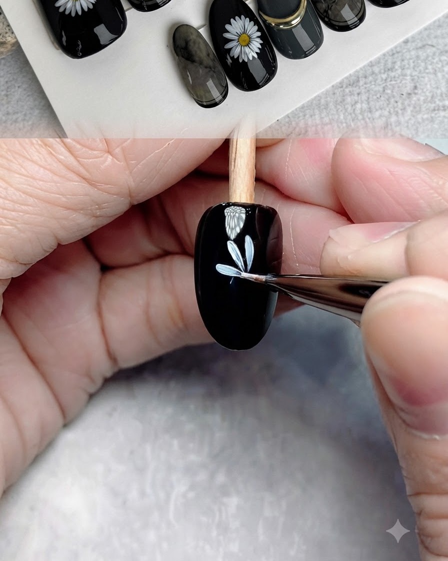 A fine detail brush adding more white petals to complete the first flower layer on a black nail.