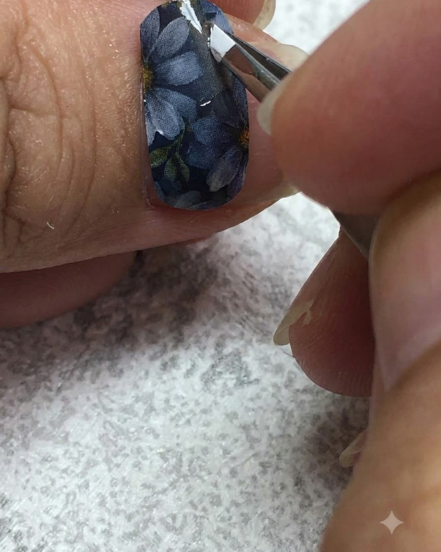 A fine liner brush carefully painting white gel onto the petals of a daisy on a grey nail.