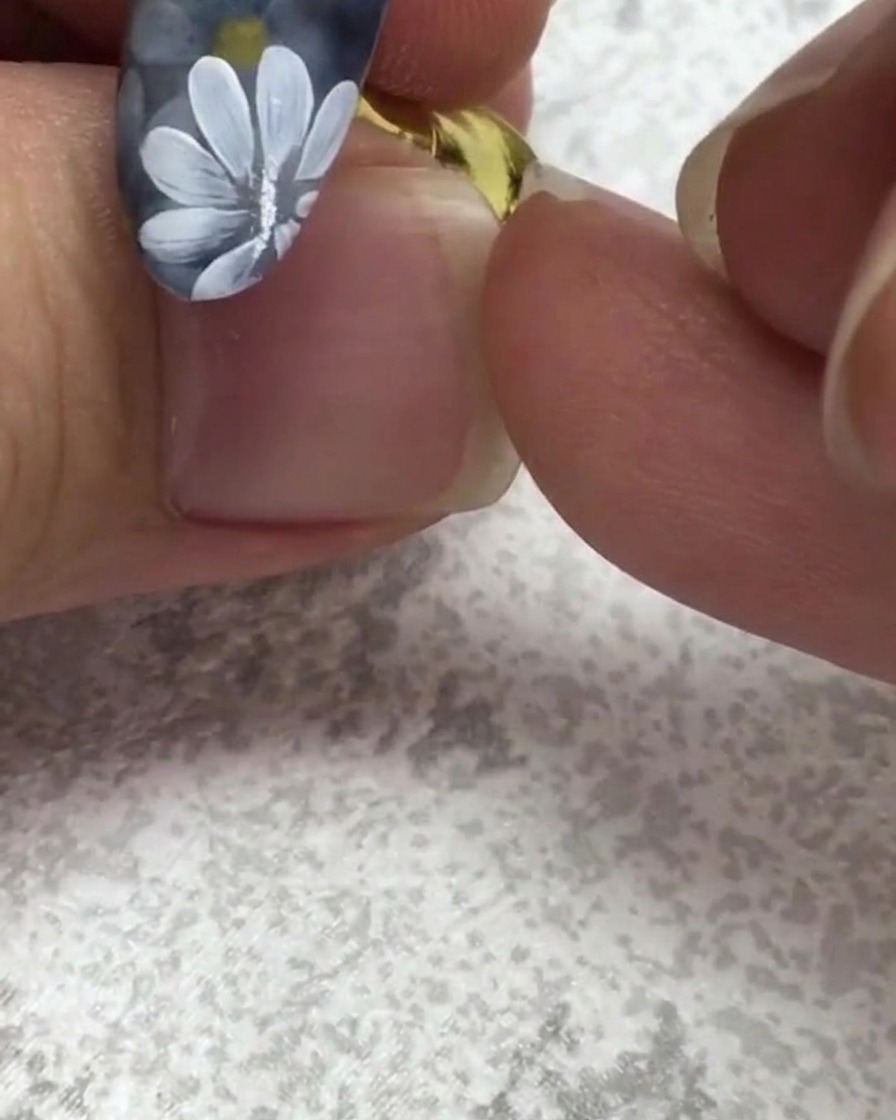 A flat nail brush picking up a small dot of green gel near a nail featuring white daisies.
