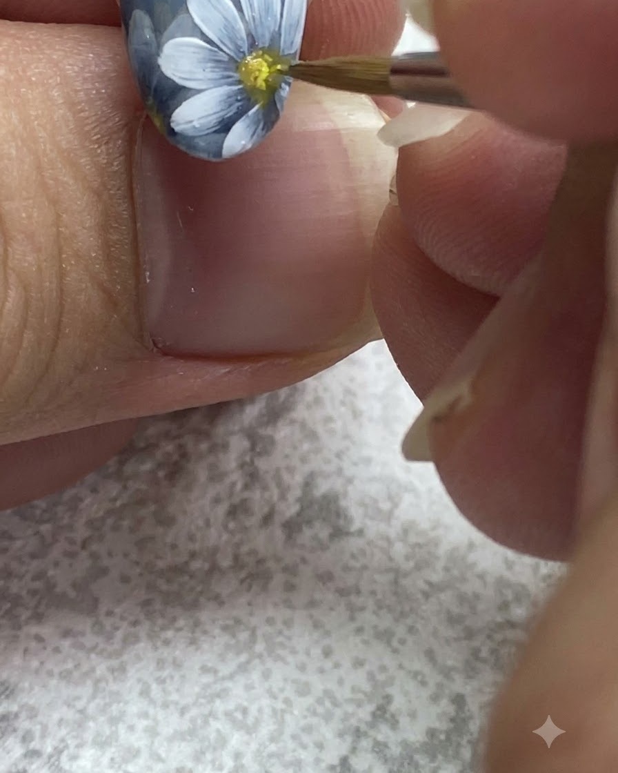 A fine brush dabbing yellow gel into the center of a painted white daisy.