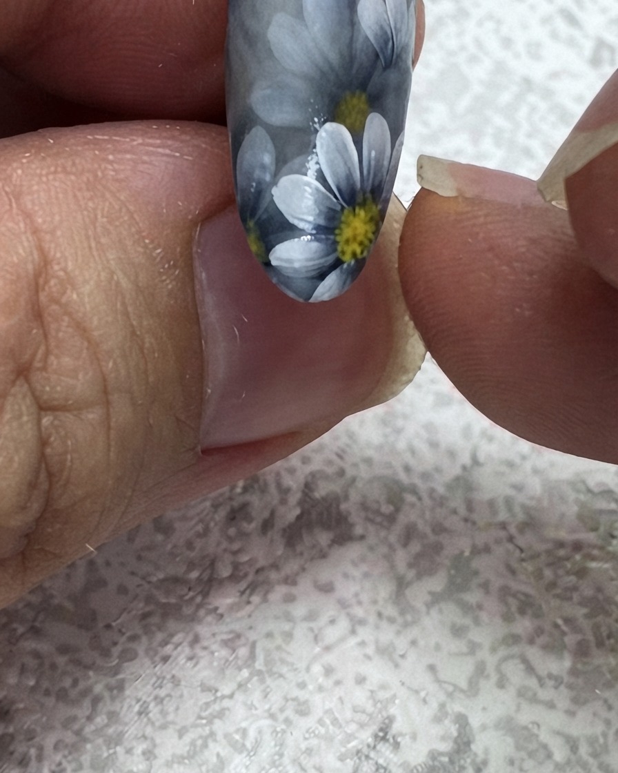 A fine liner brush adding a second green leaf to the upper corner of a floral nail design.