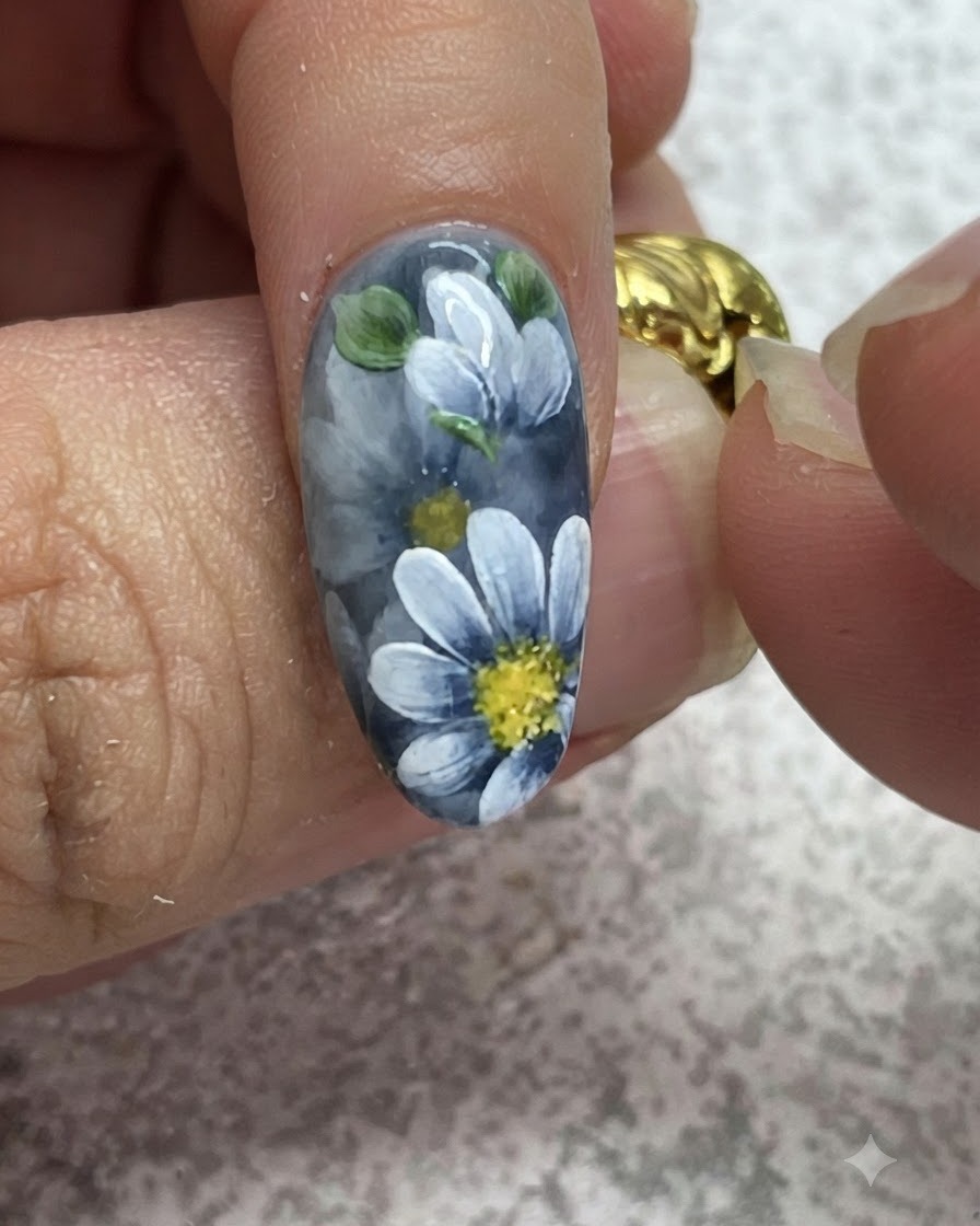 A fine brush adding detailed highlights onto painted green leaves on a grey gel manicure.