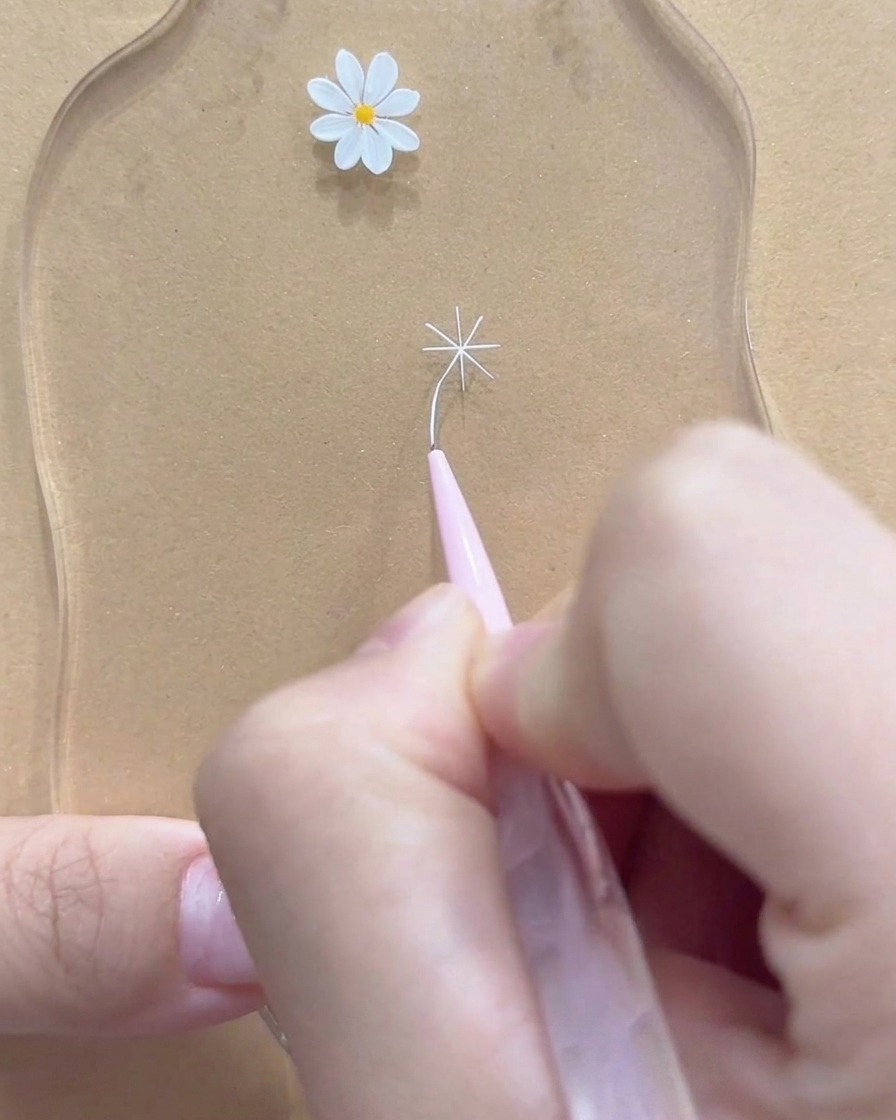 A close-up of a fine liner brush perfecting the outer tips of a white daisy flower.