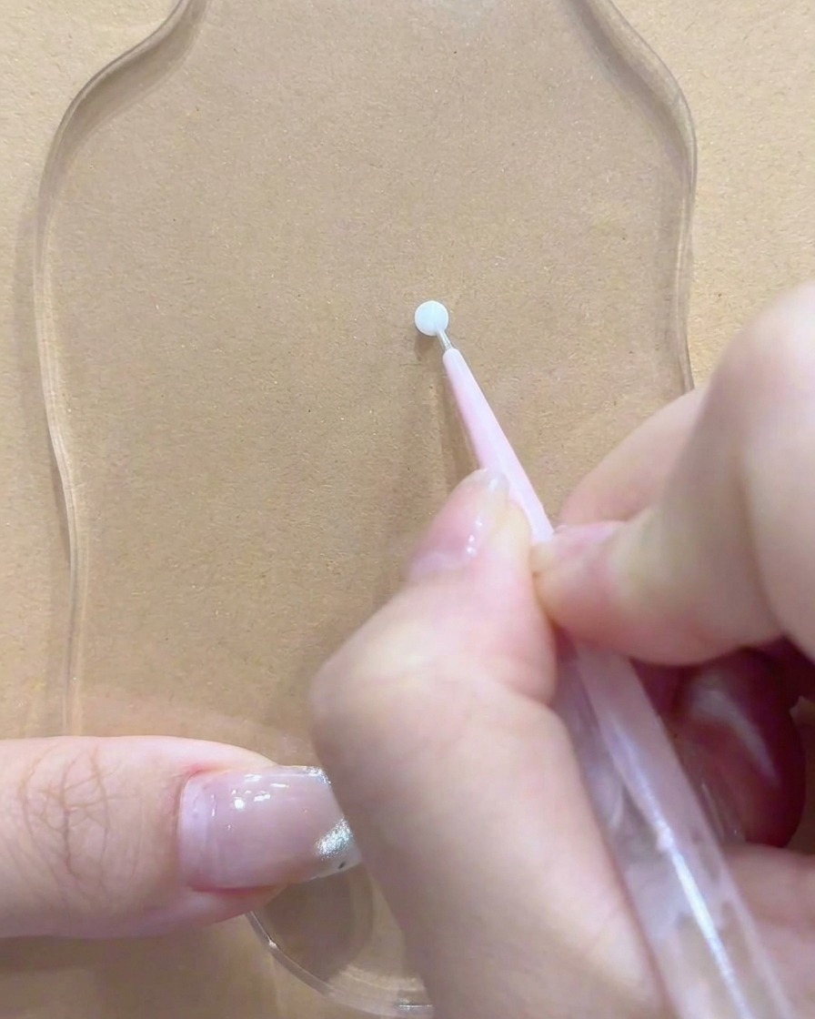 A dotting tool or brush resting near a clean spot on the clear acrylic palette.