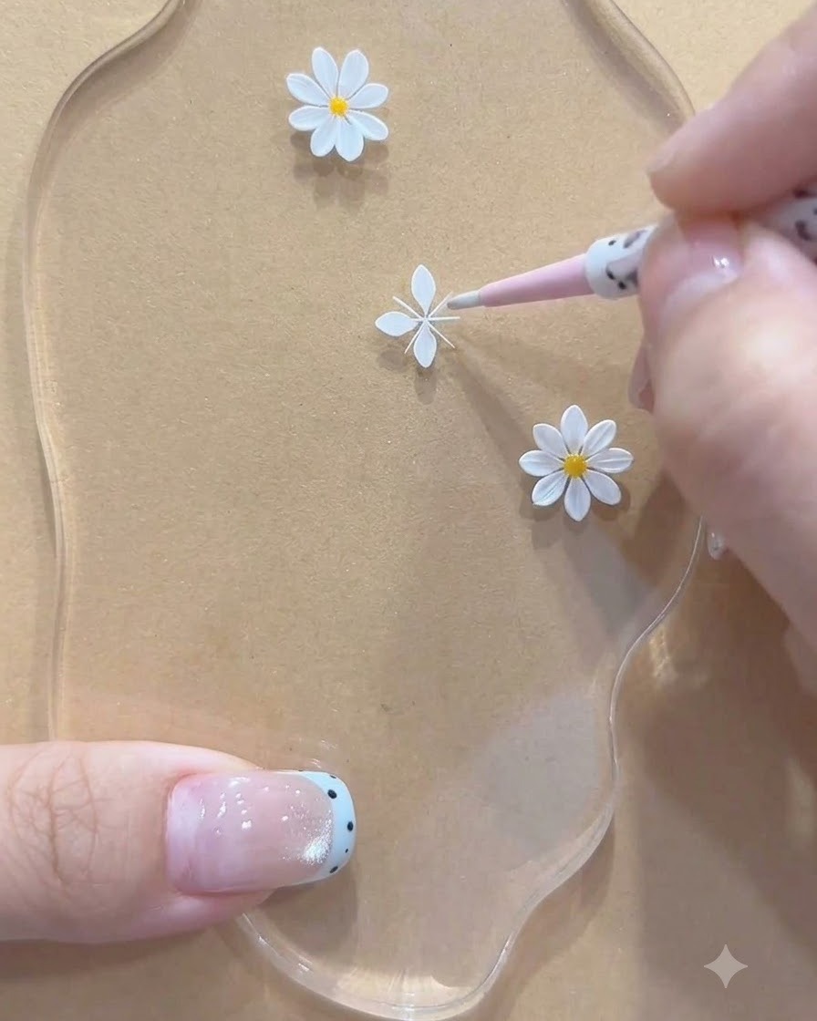 A close-up view of a pink tool adjusting white painted petal structures for a small daisy on an acrylic palette.