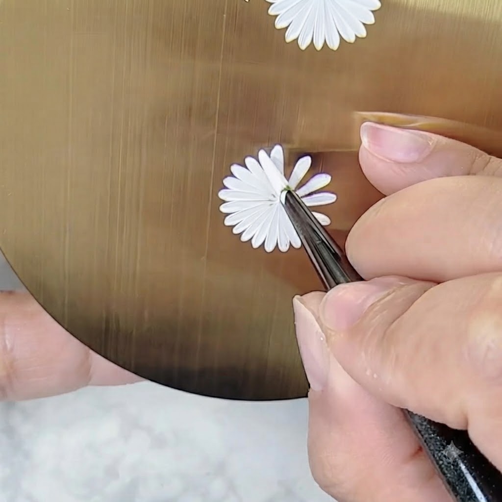 A hand holding a nail art brush at an adjusted angle to paint details on a daisy design without turning the palette.