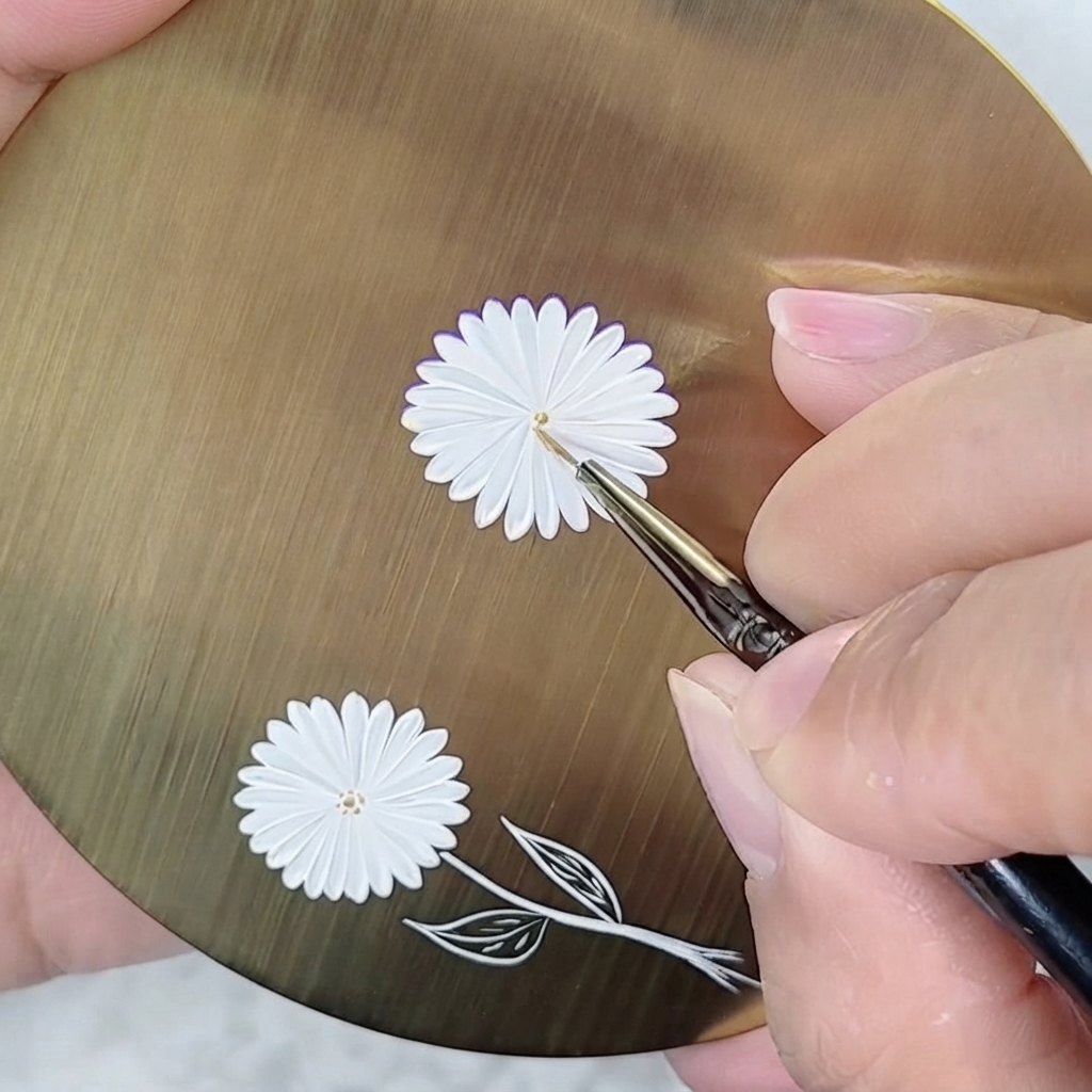 A fine-liner brush placing a tiny golden dot in the center of a white painted daisy.