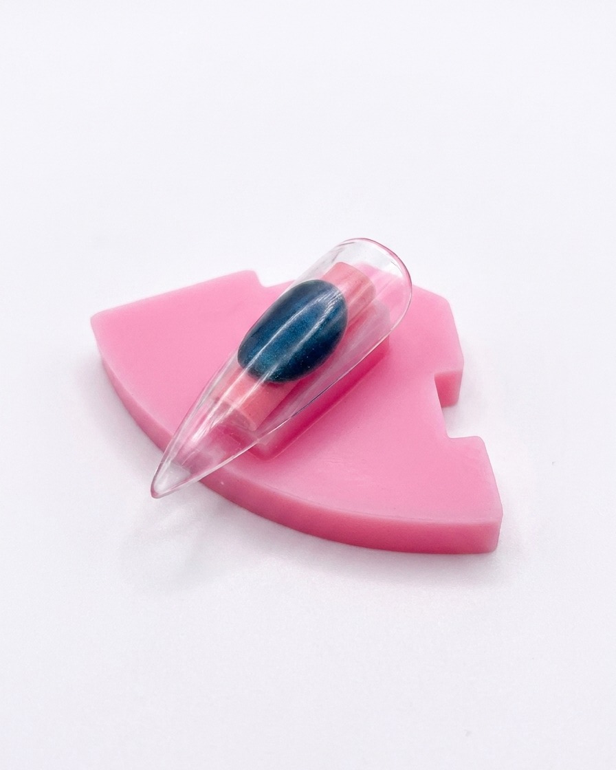 A single plastic nail tip with an aurora chrome finish displayed upright on a pink holder.