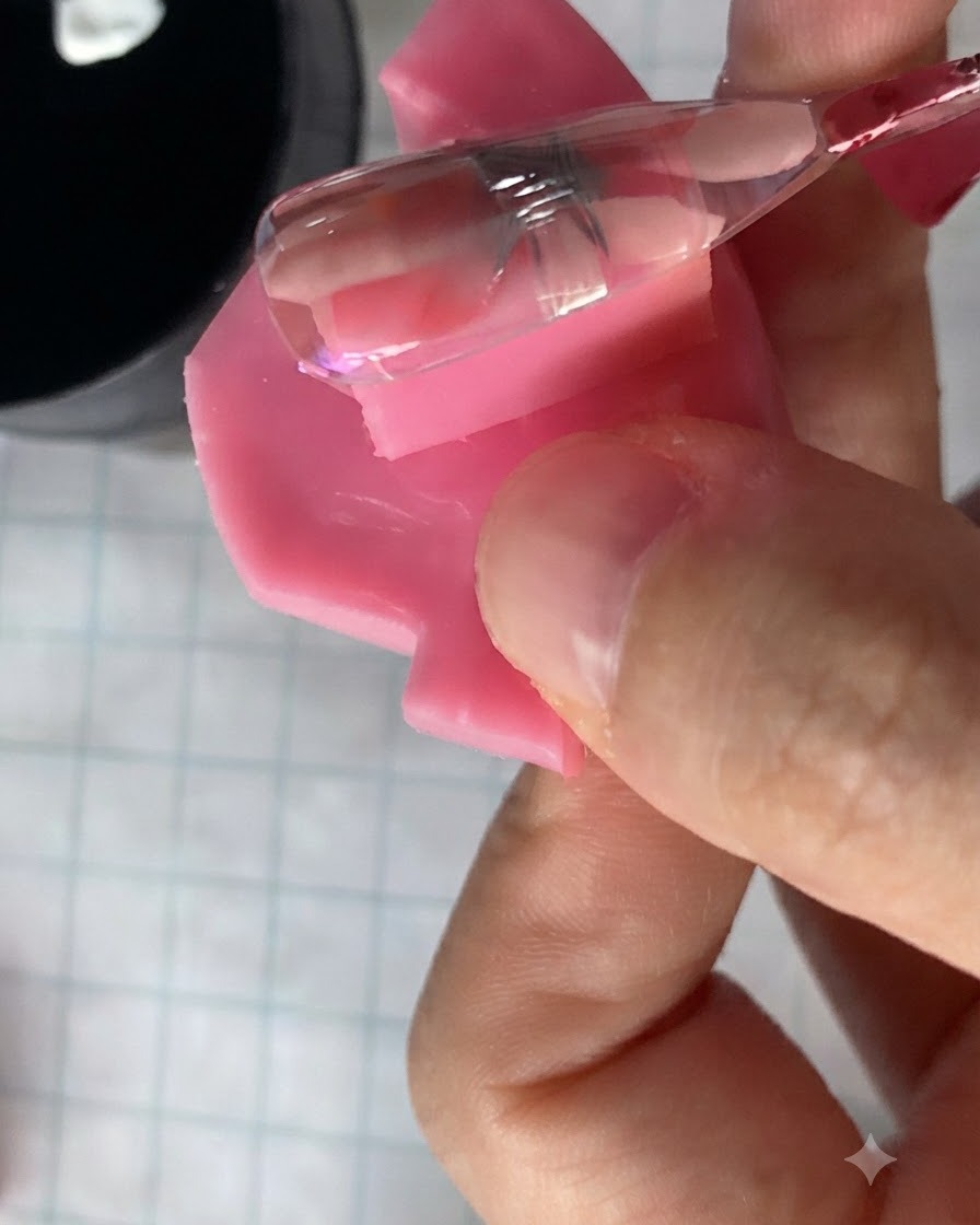 A small nail brush applying a translucent pink gel over a cured daisy flower design on a nail.