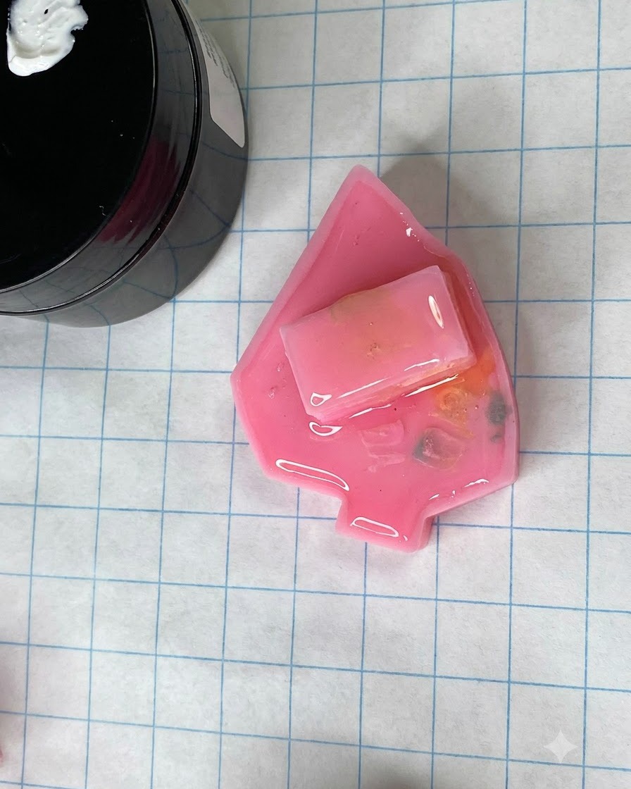 A cured matte pink nail mold resting on a grid crafting mat next to a jar of gel.