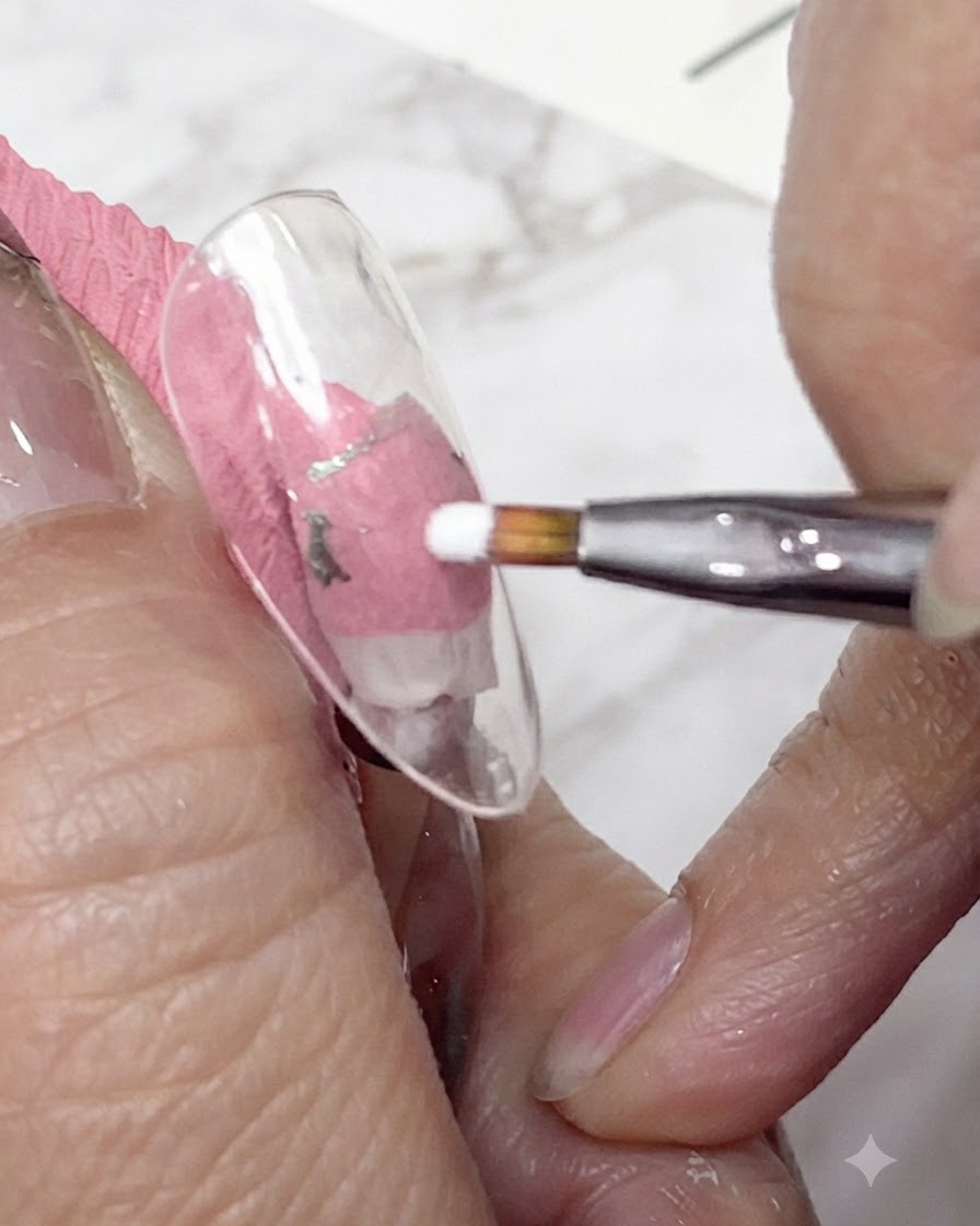 A close-up shot of a fine liner brush applying white gel to form the first petals of a daisy on a clear nail tip.