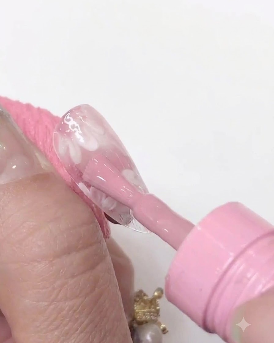 A mini UV/LED nail lamp held closely over a clear nail tip to cure the applied pink gel layer.