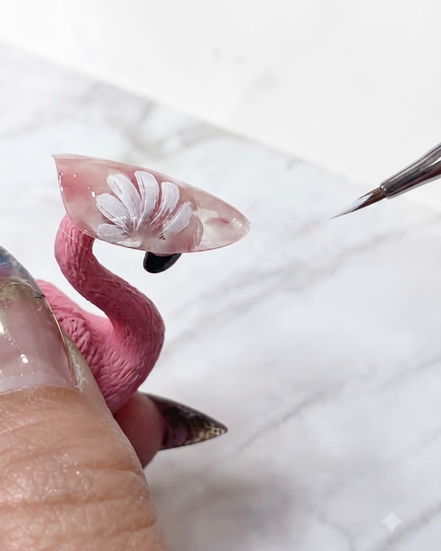 A fine nail art brush touching up the crisp white tips of layered daisy petals on a translucent pink extension.