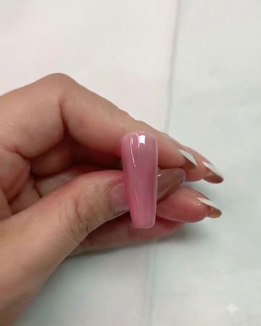 A brush applying clear matte top coat onto a glossy pink artificial nail surface.