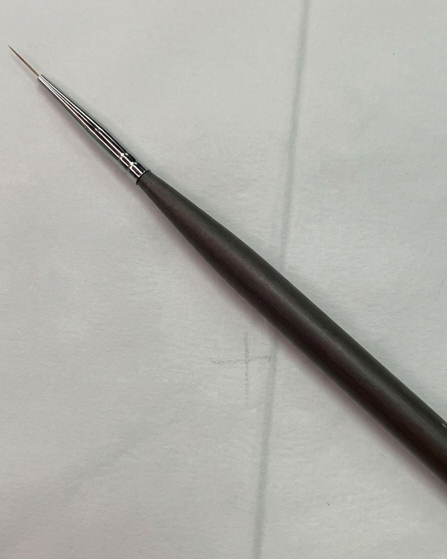 A fine nail art liner brush positioned near a light guide grid sketch on a practice nail surface.