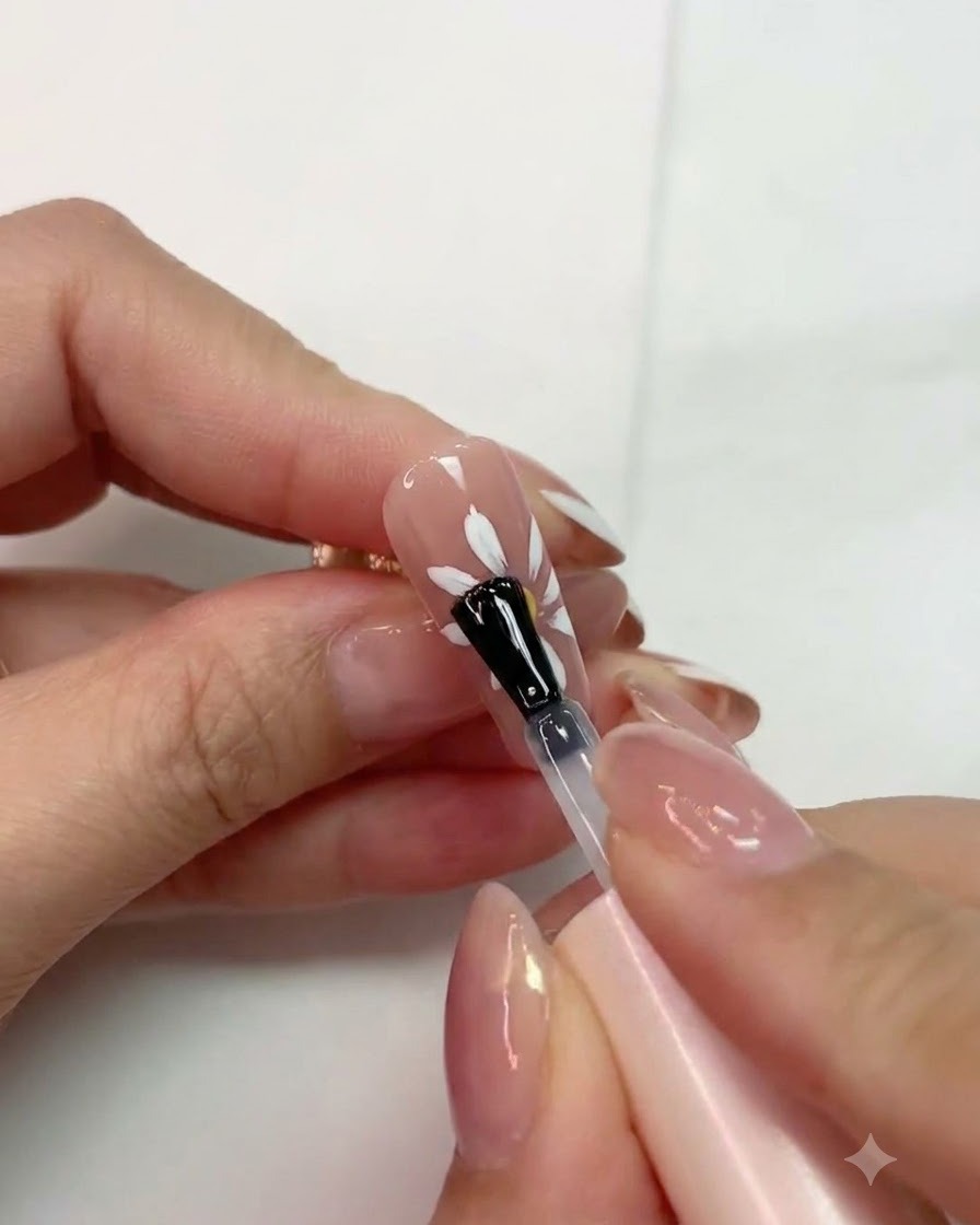 A brush applying matte top coat over a cured white daisy design on a pink nail.