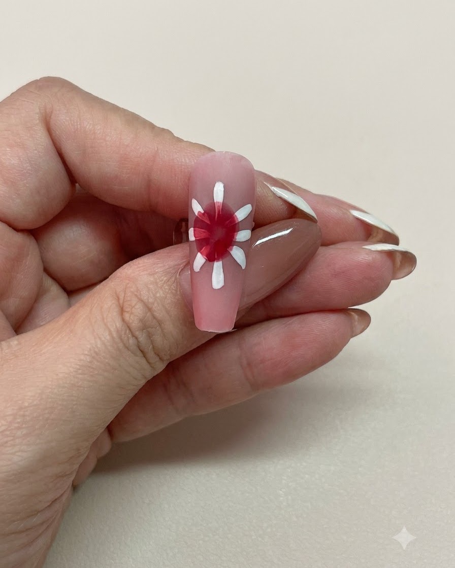 A close-up view of a pink nail with a softly diffused red blooming center surrounded by white petals.