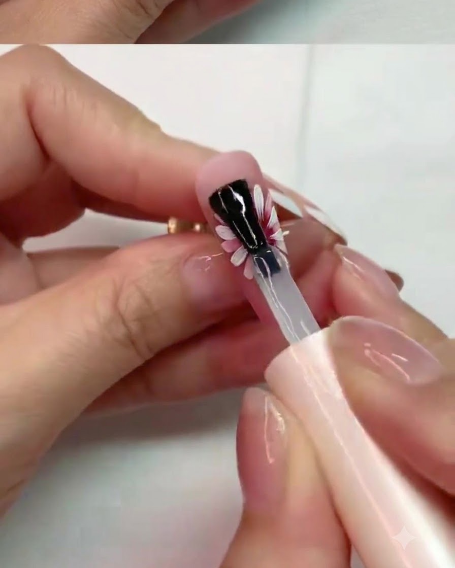 A brush carefully applying matte top coat onto the middle petals of a painted daisy nail design.