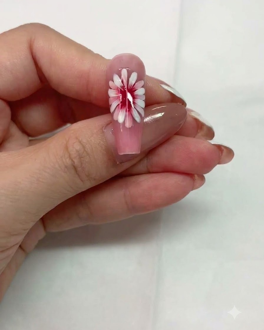 A close-up view of a pink nail with a multi-layered daisy design resting before curing.