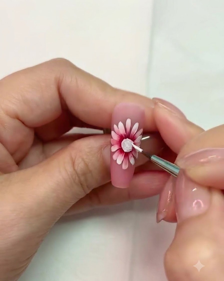 A fine brush working near the cured white textured center of the daisy nail art.