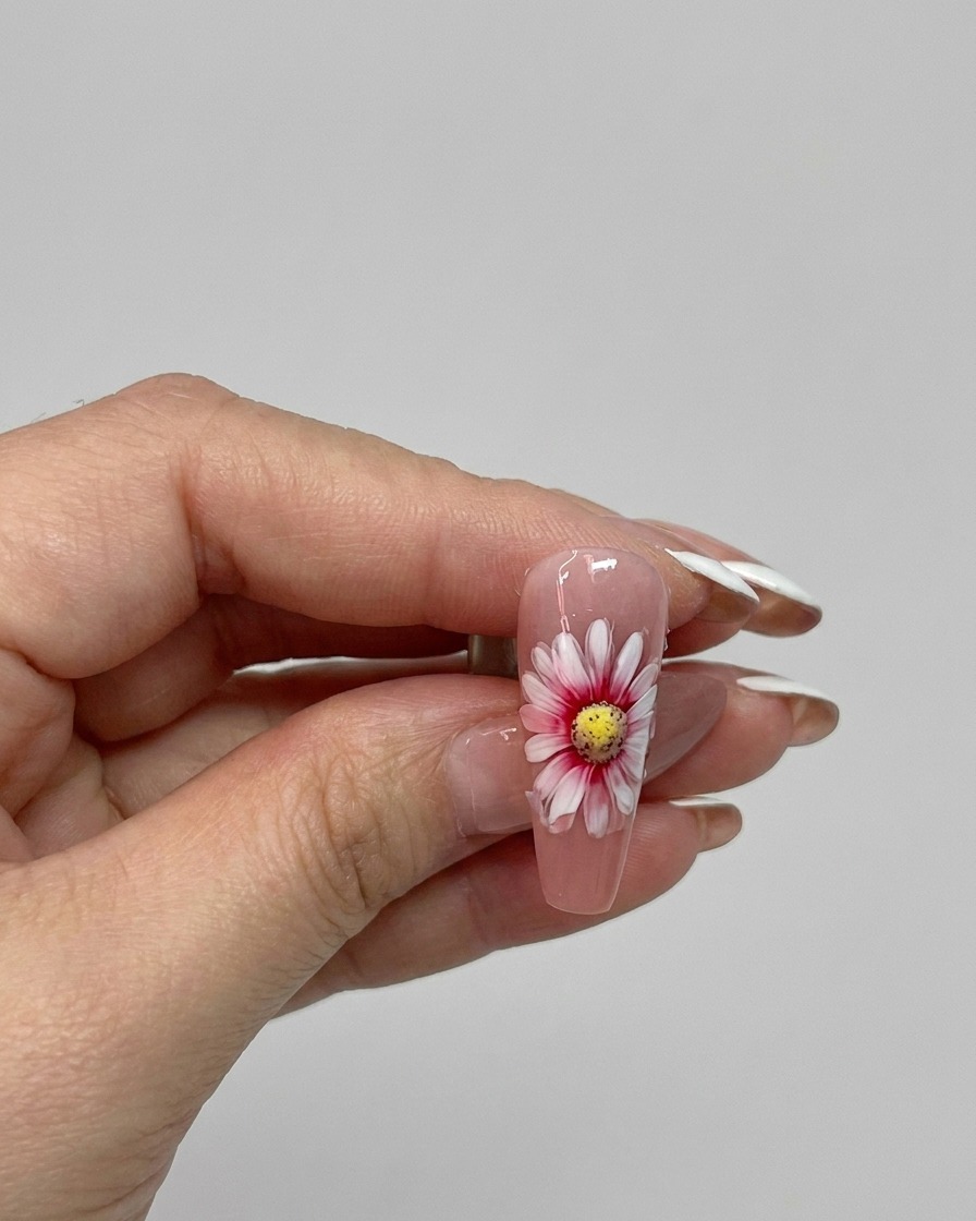 A brush applying a glossy top coat over a finished double layer daisy nail design.