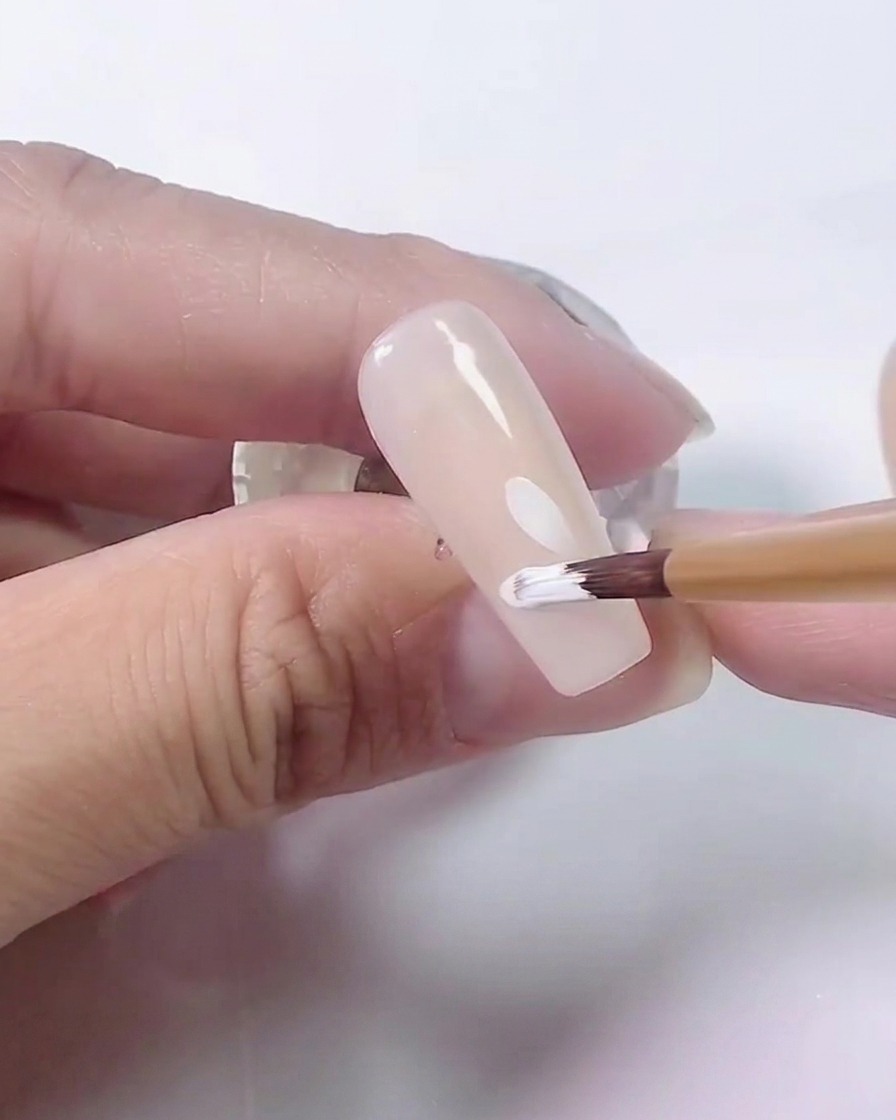 A close-up view of a brush adding more petals to the white daisy design on a nude base.