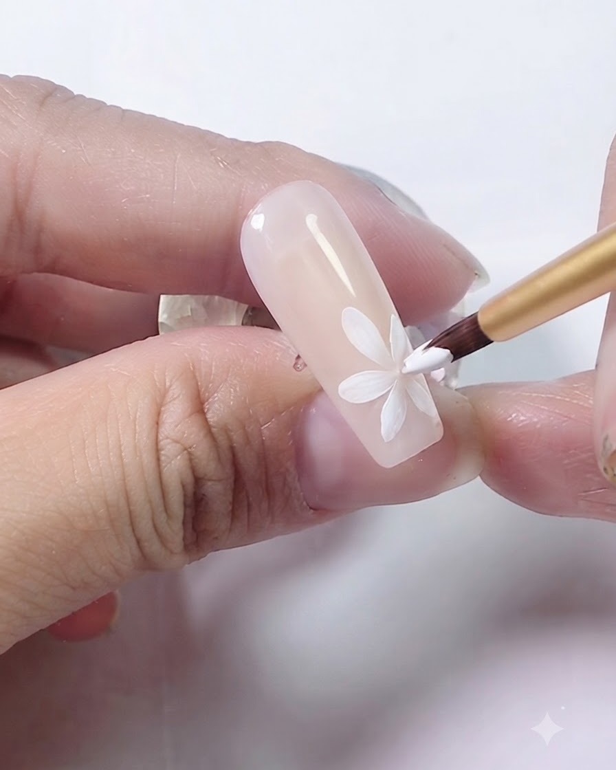 A fine brush applying an amber-colored dot to the center of the painted daisy.