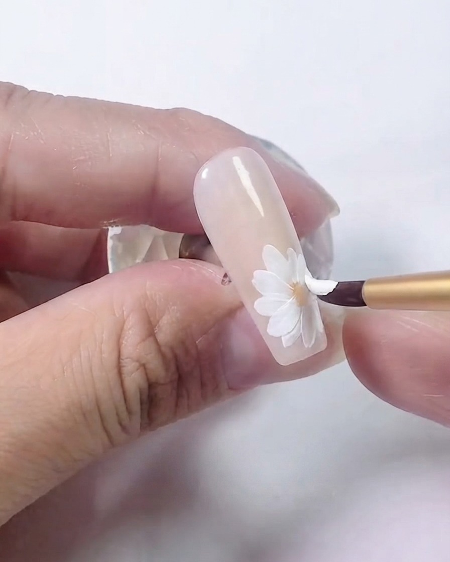 A nail brush adding a second, overlapping layer of white petals onto the daisy.