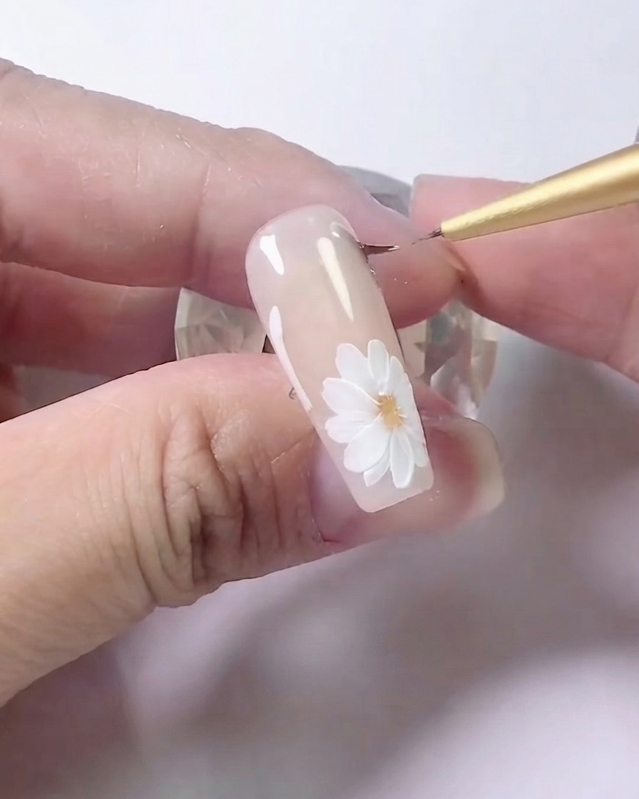A liner brush carefully blending gray shading along the side lines of a floral nail art design.