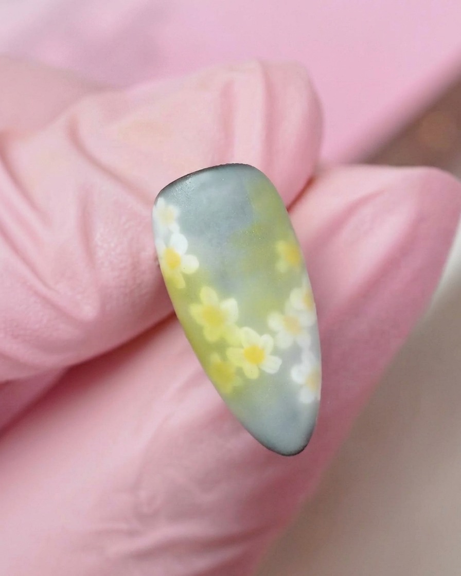 A finished view of the nail showing multiple layers of soft white daisies scattered over a muted gradient background.