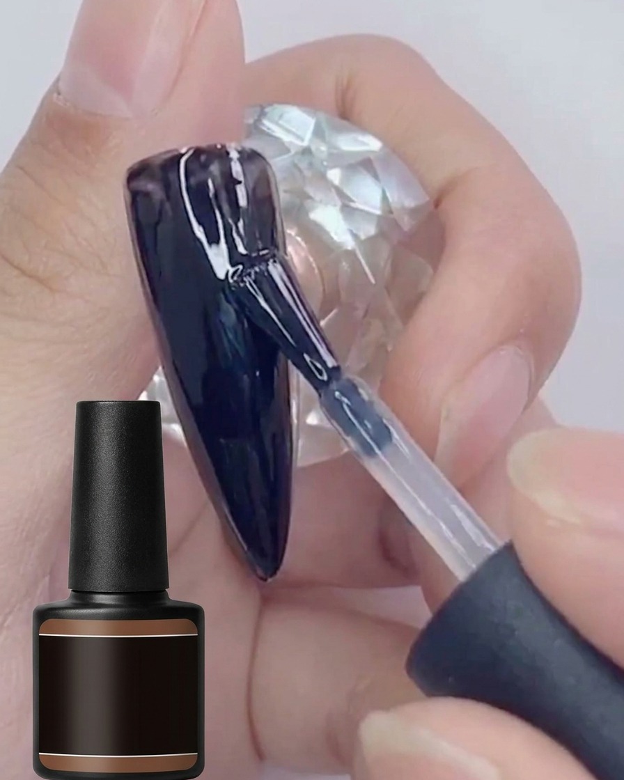 A brush applying a second coat of glossy black gel polish onto a black-painted nail surface.