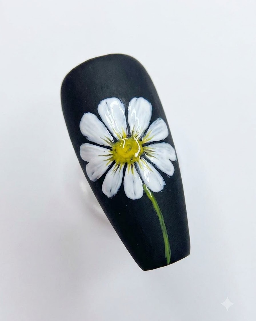 A completed black nail art design featuring a detailed white daisy with a bright yellow center and a green stem.
