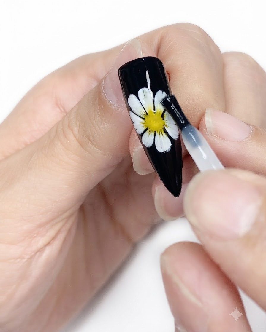 A cleansing wipe cleaning the surface of a finished black nail with white and yellow daisy art.