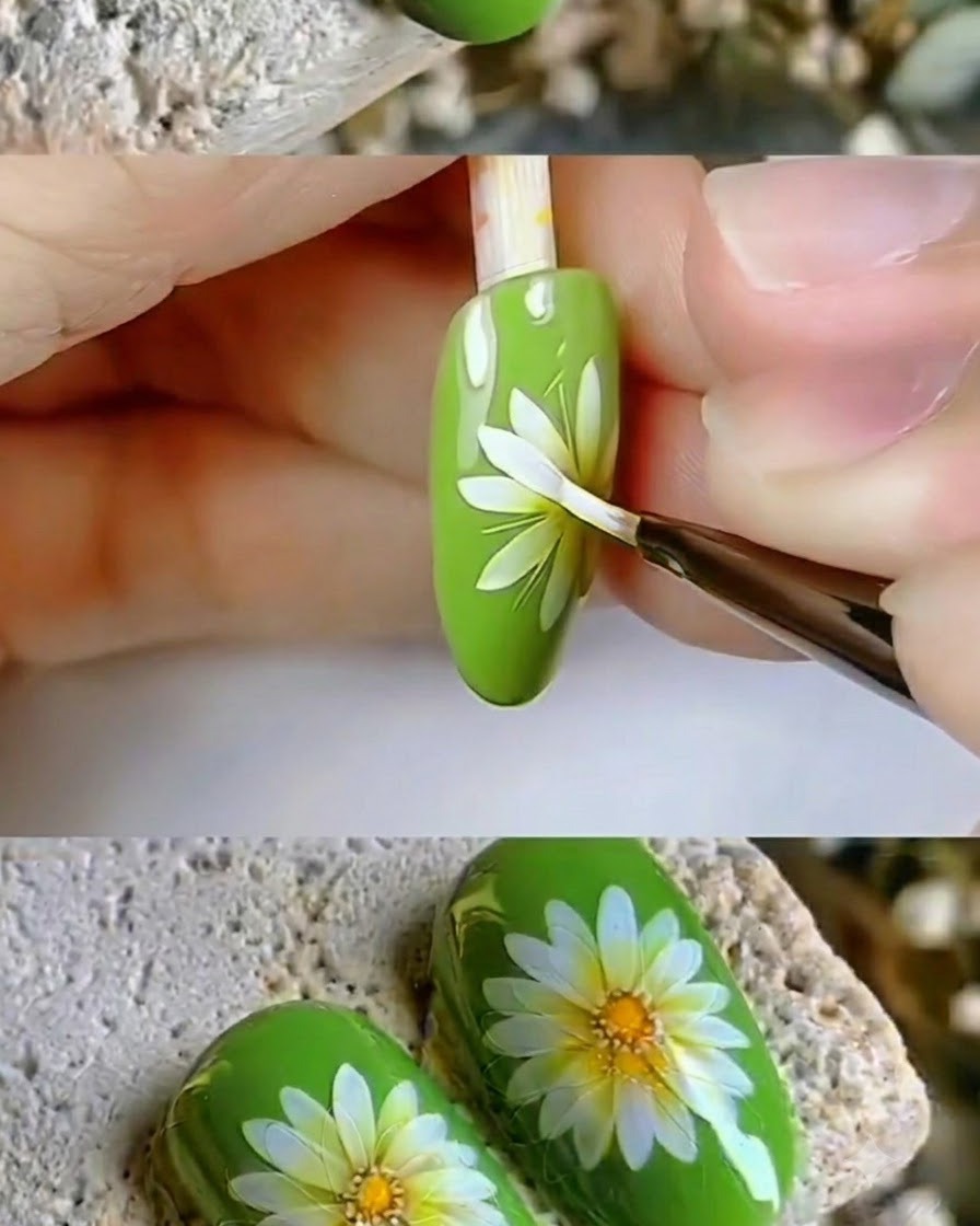 A fine detail brush touching up the crisp white petals of a daisy nail art design.