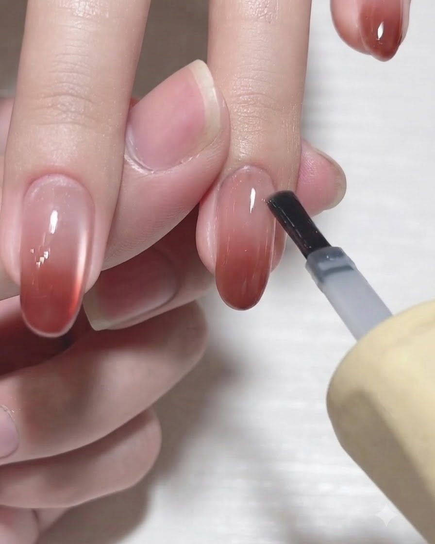 A gel bottle brush applying a glossy clear top coat over a finished gradient fingernail.