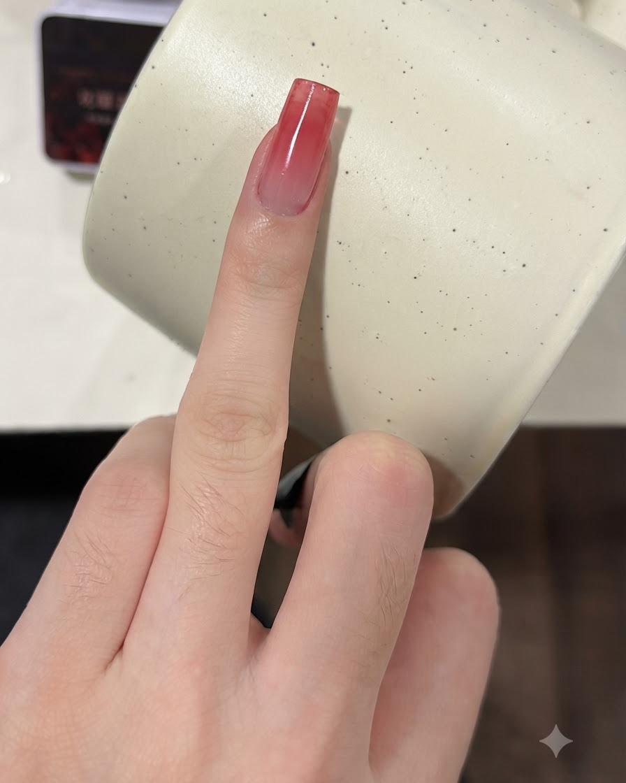A finger with a growing wine red gradient nail being pressed with a sponge for a second coat.