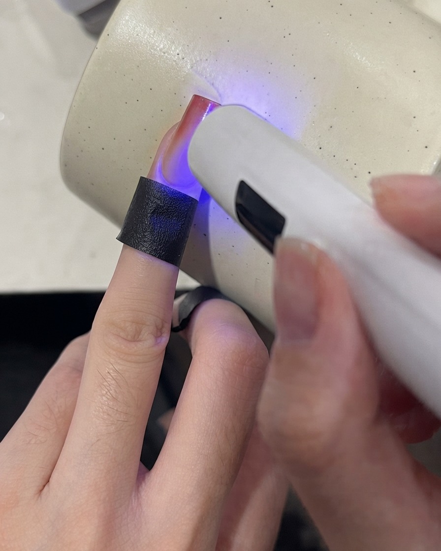 A mini UV lamp curing the tip of a gradient nail with a wine red finish.