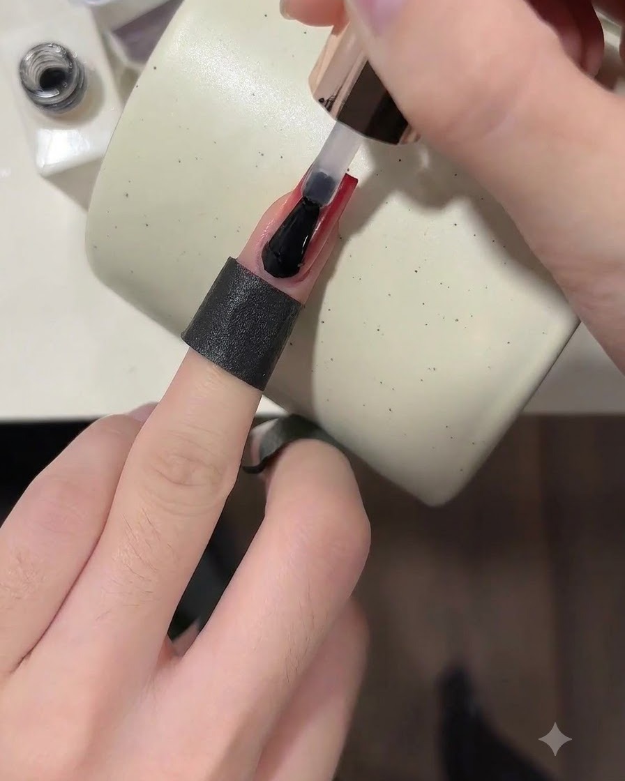 A brush applying a clear glossy top coat over a finished wine red ombre nail.