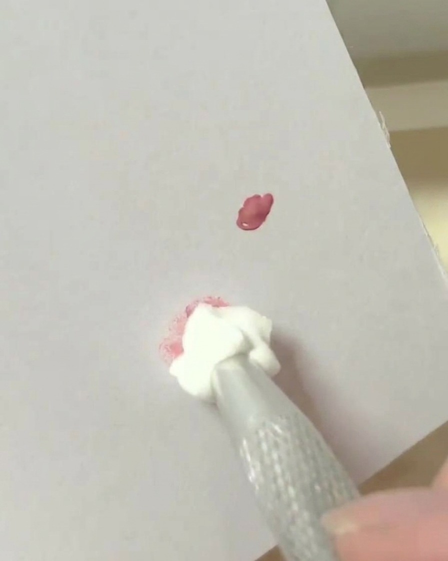 A makeup sponge tool dabbing into a mixed pigment spot on a white palette surface.