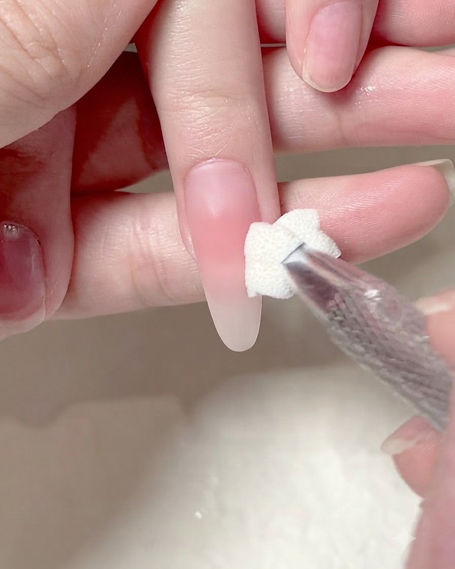 A sponge applicator dabbing a second layer of pink gel onto the center of a manicured nail.